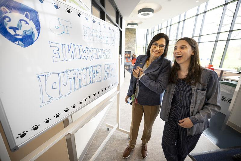 两个女人站在一块写着欢迎欧博官网app下载的白板旁边.